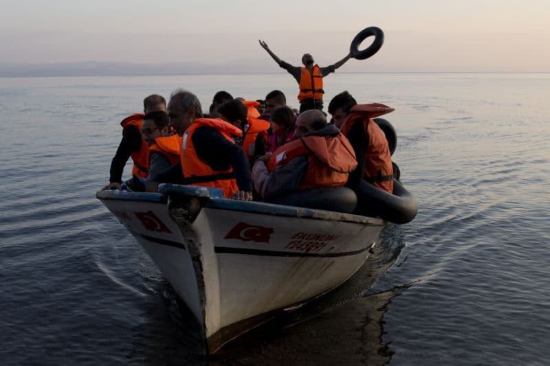 Uprchlí vzdávající dík bohu za úspěšné zdolání cesty po Egejském moři na rybářském člunu z Turecka na řecký ostrov Lesbos.