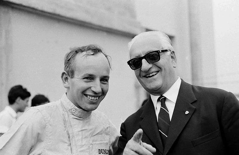 Zakladatel slavné automobilky Enzo Ferrari. Vlevo je britský závodník F1 John Surtees. Snímek je z roku 1964.