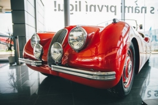 Velmi vzácný Jaguar XK 120 Alloy Roadster 1949 - s hliníkovou karoserií bylo ručně vyrobeno pouze 242 kusů (z toho 184 s levostranným řízením), a to na počátku výroby tohoto modelu, dokud výrobce z kapacitních důvodů nepřešel na ocelovou karoserii, což umožnilo rychlejší výrobu a tím uspokojení nečekaně velké poptávky. Rané hliníkové exempláře jsou nejen lehčí, ale vzhledem k mnohem menšímu počtu vyrobených kusů (242 z celkového počtu 7631 vyrobených XK 120) také výrazně cennější. Tento konkrétní exemplář prošel v druhé polovině 80. let kompletní náročnou renovací provedenou na špičkové úrovni dle tehdejších standardů. Autenticitu vozu (výrobní číslo podvozku + karoserie + bloku motoru + převodovky, původnost barevného odstínu i barvy interiéru = vše zachováno tak, jak bylo auto v roce 1949 vyrobeno) dokládá certifikát Jaguar Heritage Trust. Po dokončení renovace tento konkrétní vůz získal několik vrcholných ocenění na výstavách a přehlídkách (např. v roce 1989 na prestižní akci Jaguar Club North America získal skóre 99.36 a titul Best of Show a Best of Class winner). Vůz dovezen z USA, v ČR zatím neregistrován, vystaven na pražské centrále AAA AUTO.